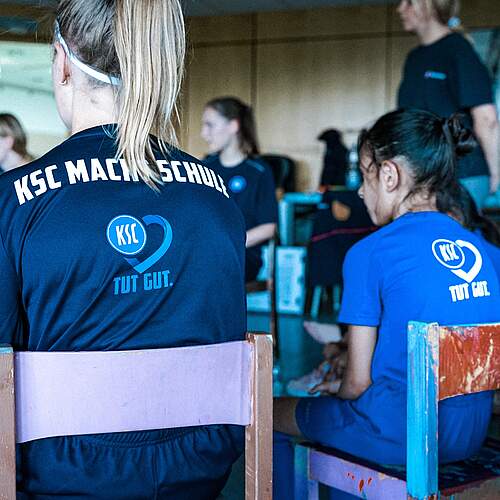 Zwei Mädchen sitzen auf Stühlen und tragen Shirts von KSC macht Schule.