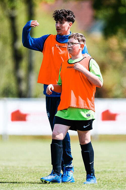 U15-Spieler und Kind der Sozialeinrichtung halten zusammen