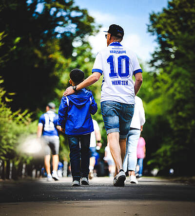 Ein Vater im KSC-Trikot läuft mit seinem Sohn durchs Grüne.