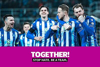 KSC-Spieler jubeln gemeinsam im Heimtrikot. Darüber hinaus wird die Botschaft des Aktionsspieltags "TOGETHER!" abgebildet. Diese lautet "STOP HATE. BE A TEAM.".