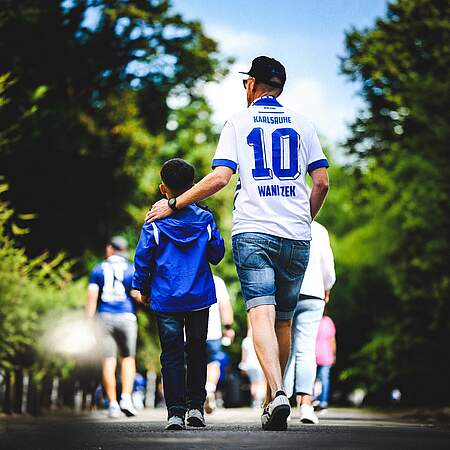 Ein Vater im KSC-Trikot läuft mit seinem Sohn durchs Grüne.