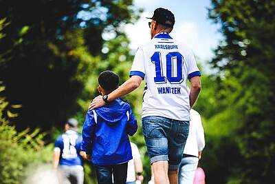 Ein Vater im KSC-Trikot läuft mit seinem Sohn durchs Grüne.