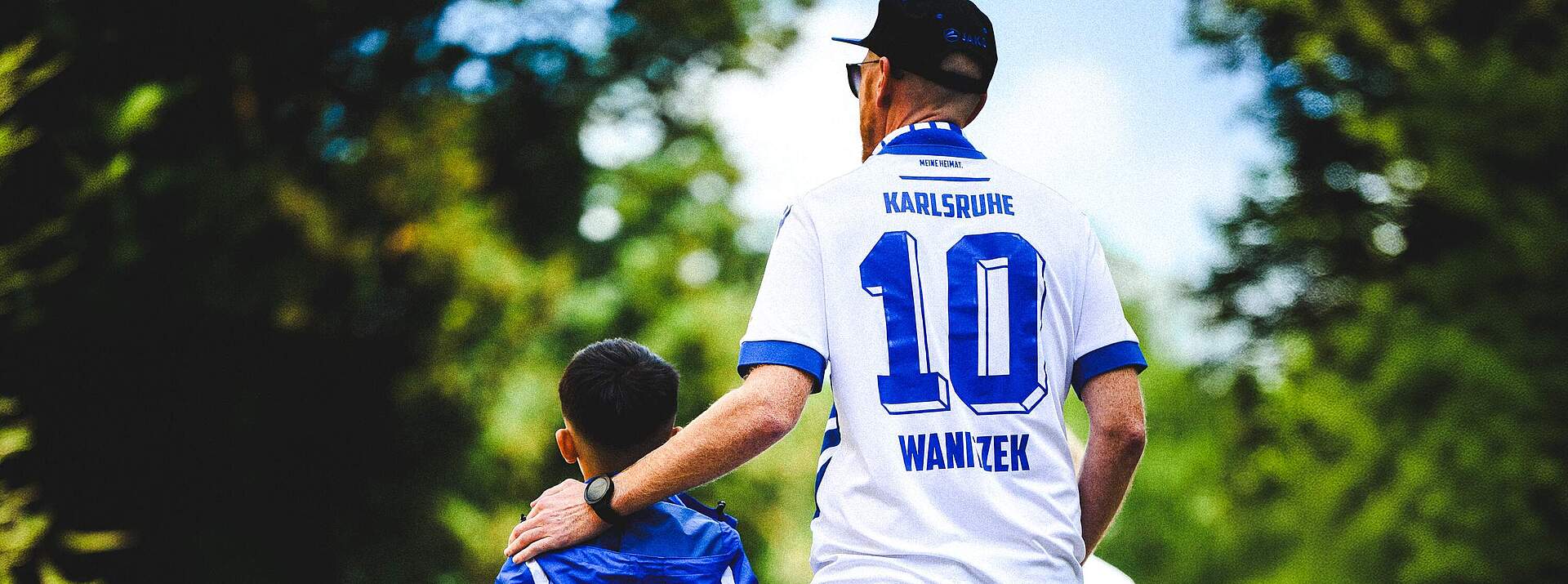 Ein Vater im KSC-Trikot läuft mit seinem Sohn durchs Grüne.