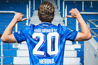 David Herold zeigt im Heimtrikot auf den Flock auf dem Rücken