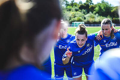 Die KSC-Frauen bilden einen Mannschaftskreis und eine Spielerin hebt ihre Hand und spricht zur Mannschaft.