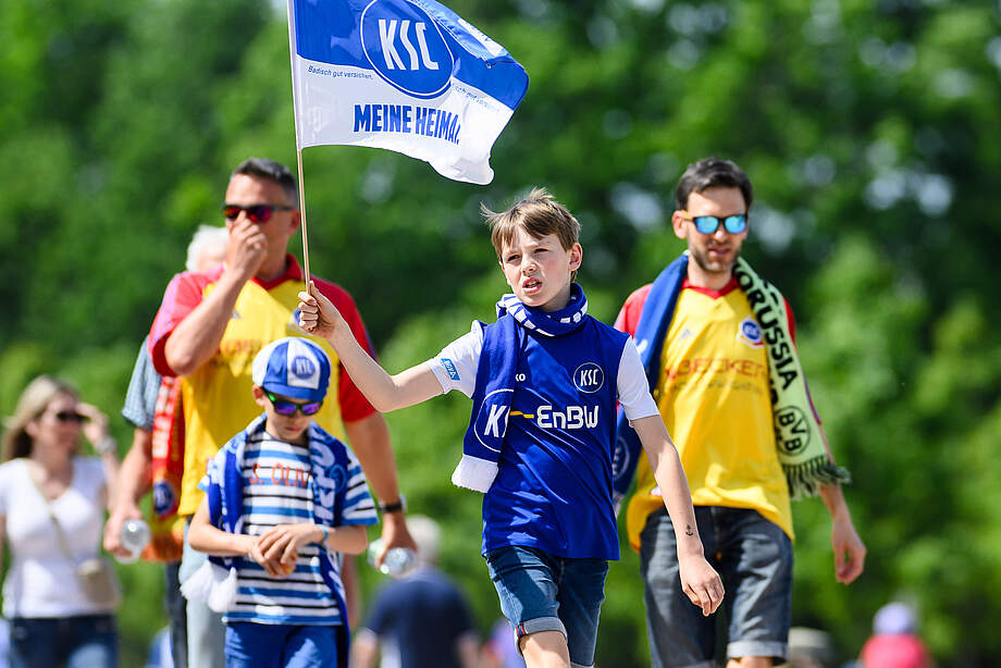 Ein Junge im KSC-Trikot schwenkt eine blau-weiße "Meine Heimat."-Fahne